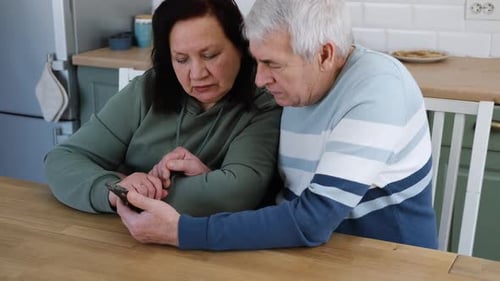 Senior couple look at smartphone in kitchen together