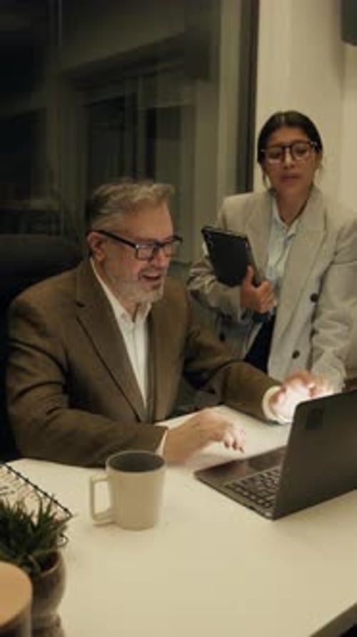 Two Multiethnic Colleagues Collaborating on Business Report in Office at Night