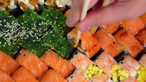 Japanese kitchen with sea food. Putting one sushi roll from set using sticks for sushi. Hand hold
