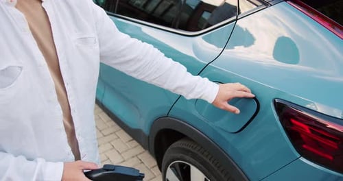 Nahaufnahme eines Mannes, der ein Elektroauto für das Aufladen vorbereitet, indem er den Anschluss öffnet und das