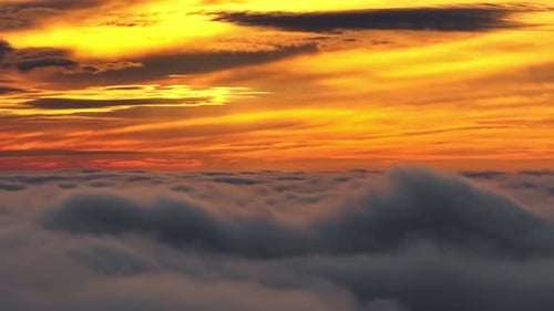 Dramatic orange sunset sky above thick rolling clouds at high altitude in aerial view