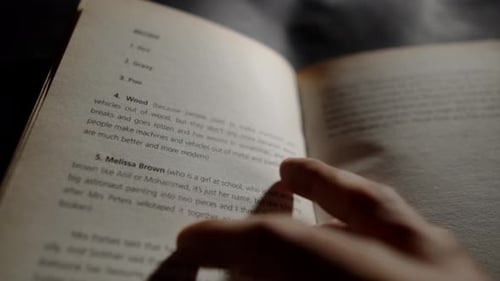 close-up of a hand turning the page of a book with text on the pages in focus, and the words clearly