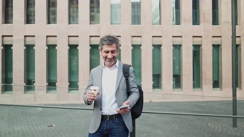 Smiling Man Drinking Coffee Checking Phone in Urban Setting