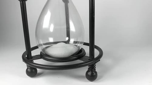 The bottom part of an hourglass with black metallic base filling up with white sands of time, ISOLAT