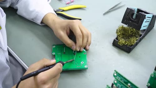 Soldering a Green Circuit Board in Workplace