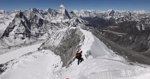 Person walking on the summit of Island Peak in Nepal with views of surrounding mountains.