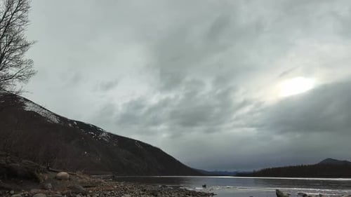 A timelapse video showcasing an overcast day by the river. The background features mountains partial