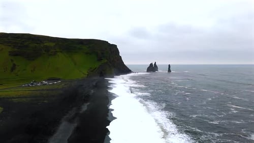 The drone footage showcases Reynisfjara’s iconic basalt sea stacks, standing tall against the wild o