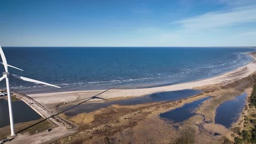 Aerial footage of wind turbine on the sea near industrial zone and harbor.