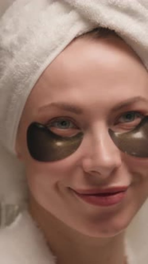 Woman Applying Eye Patches in Towel and Robe