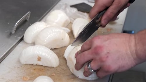 A close up shot of half onions being chopped into slices by hand.