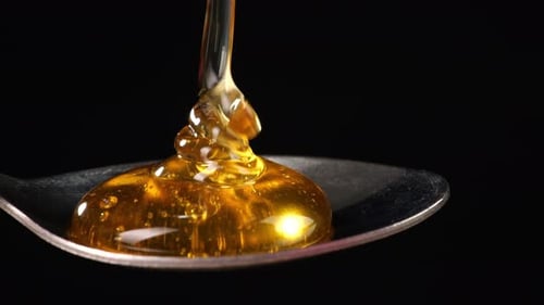 Honey Pouring To Spoon On Black Background. Organic Thick Honey Sweet Dessert