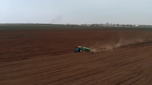 Tractor with Sowing Mechanism Moves Across Field and Sows Ground with Sunflower Seeds Near Farm