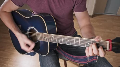 Man Plays Acoustic Guitar, Seated Indoors