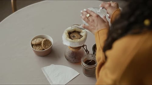 Woman Preparing Coffee at Table with Cookies