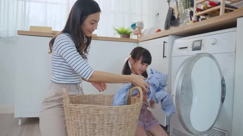 Asian beautiful mother teach young daughter wash dirty clothes at home.