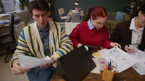 Coworkers Analyzing Business Papers Using Digital Devices at Office Desk
