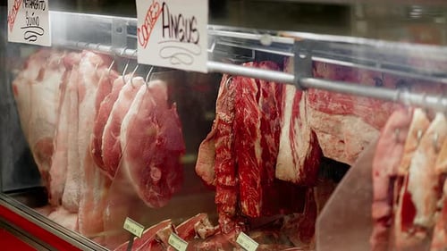 A display of meat in a store with a sign that says "Angus". The meat is hanging from hooks and it is