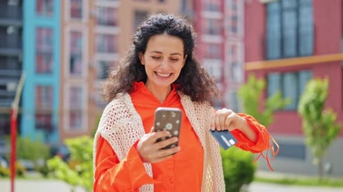 Happy Woman Making Online Payment Using Credit Card and Phone Outdoors