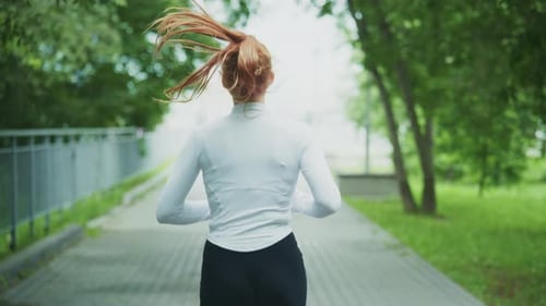 A Young Woman Jogs Energetically Along a Treelined Path Showcasing Determination and Fitness As She