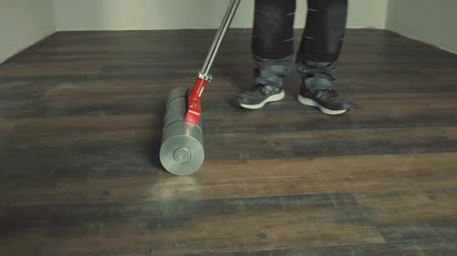 Worker using heavy roller to install vinyl laminate flooring
