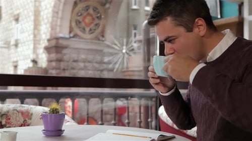 Brunette Man Sipping Coffee While Writing in a Cozy Cafe