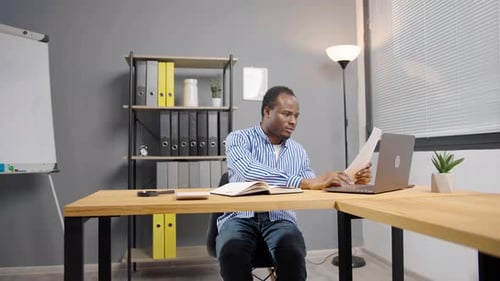Man Works at Desk with Laptop and Paperwork