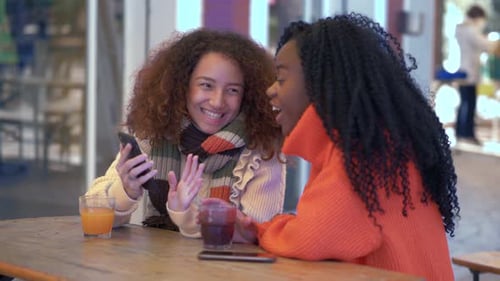 Two Friends Laughing at Phone in Cafe