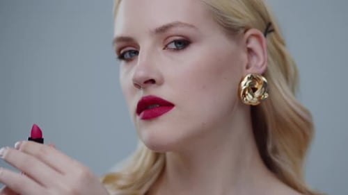 An Elegant Woman Dressed in Fashionable Accessories is Applying Lipstick with Style