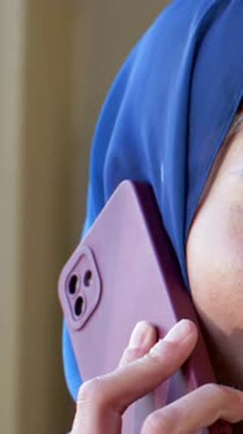 Vertical video: Phone ringing woman in blue hijab holding maroon phone to ear, ring, copy space