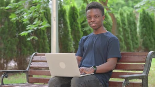 Casual African Man Smiling with Laptop in Park