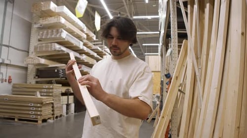 Worker Studies Lumber Beam Details in Construction Market Rack Area He Lifts Board to Eye Level Near