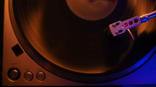 Nahaufnahme des Stylus (Nadel) eines Vinyl-Players, der in einer farbenfrohen Innenraumszene spielt.