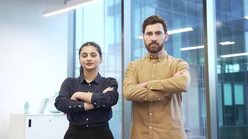 Portrait of two serious co-workers man and woman standing in modern glass office with arms crossed