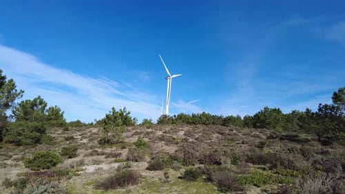 Two wind turbines spinning with green landscape in foreground and blue sky above