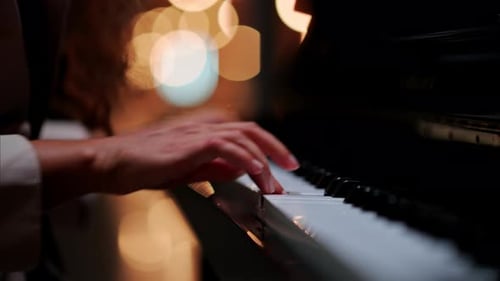 Close up of a woman's hands playing the piano with blurry lights on the background