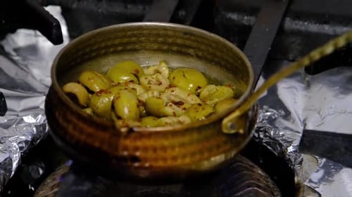 the cook is cooking oil and olives in a saucepan on the stove