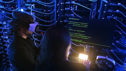 Woman programming in a server room while a man is using a Virtual Reality headset