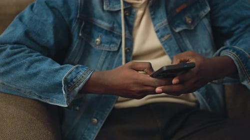 Close Up of Man Using Smartphone While Seated in Denim Jacket and Hoodie