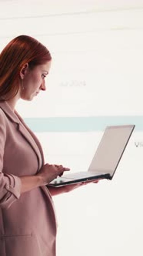 Vertical Video Businesswoman Uses Charts on Display and Laptop to Compare Profit Data