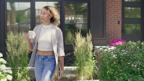 Young africanamerican woman walking with coffee outside her house on a sunny day