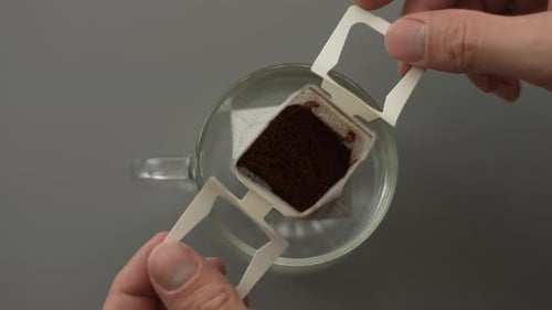 Top View of Unrecognizable Man Carefully Placing Drip Coffee Bag Into Clear Glass Cup Ready to Brew