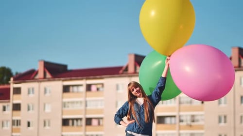 A Girl Happily Poses with Large with Colorful Balloons in the City
