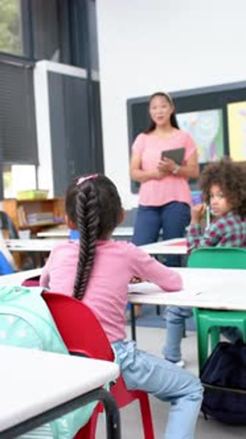 Vertical video: In school, student raising hand to ask question while teacher holding tablet