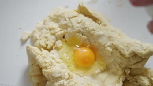 Hands Adding Egg to Dough in Bowl for Baking