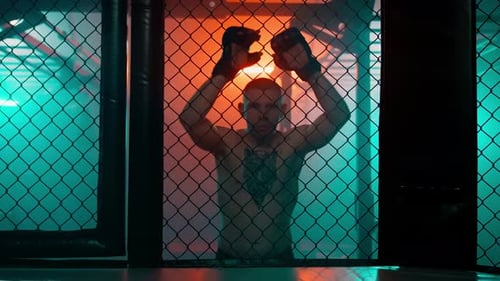 Shirtless Fighter Grips Cage with Gloves