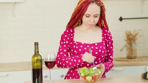 Woman Eating Salad and Drinking Wine in Kitchen