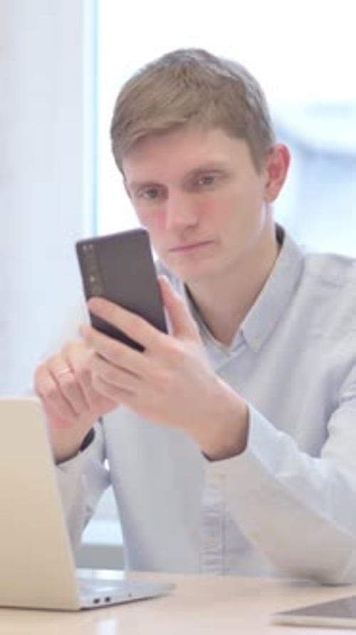 Young Man Using Smartphone and Laptop Indoors