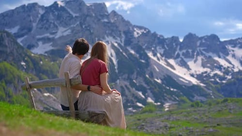 A Young Couple Dressed in Casual Clothing Sits on a Wooden Bench Gazing Out at a Picturesque Valley
