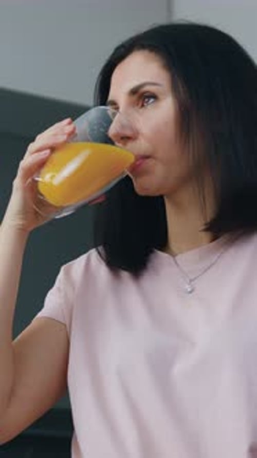 Woman Drinks Orange Juice from Glass Indoors Portrait